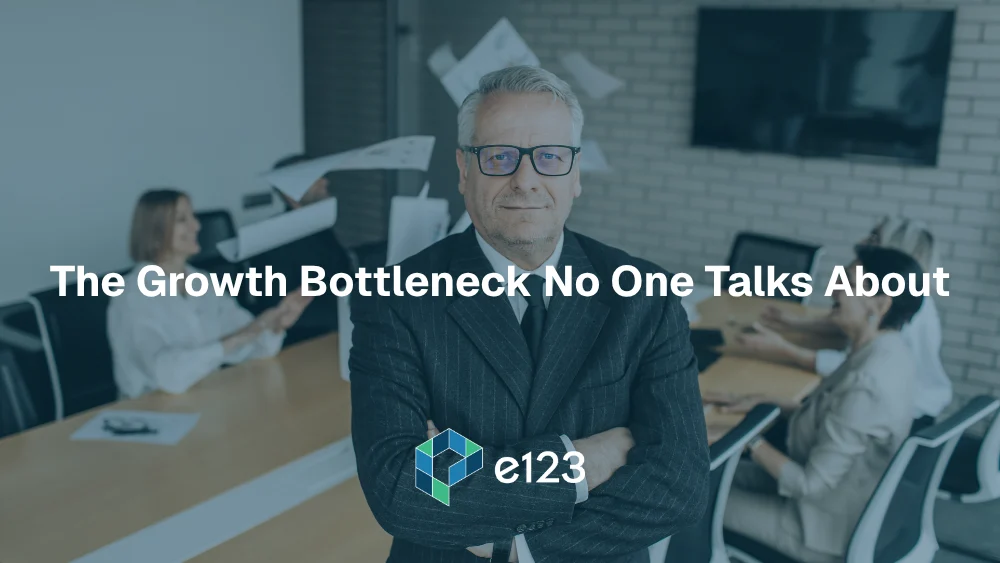 A confident older man in a suit stands with arms crossed in a conference room. Three colleagues work around a table behind him. Overlaid text reads, The Growth Bottleneck No One Talks About. The e123 logo appears at the bottom, highlighting business growth.